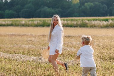 Sarışın küçük çocuk samanlı, beyaz saçlı annesiyle oynuyor. Yaz, güneşli hava, çiftçilik. Mutlu çocukluk. aile.