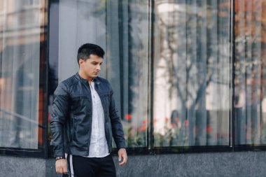 Gözlüklü, siyah deri ceketli, cam arka planda genç, şık bir adam.