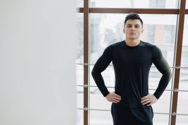 Pencere kenarındaki çekici sporcu. Sporcu geniş pencerelerin yanında poz veriyor. Spor ve spor. güneşli.