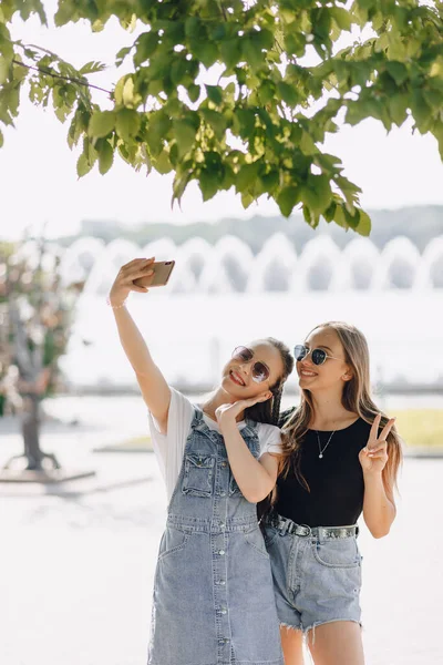 Két Fiatal Csinos Lány Sétál Parkban Képeket Készítenek Magukról Telefonban — Stock Fotó