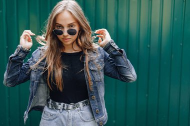 Kot elbiseli, gözlüklü, koyu yeşil arka planda mesaj atmak için boş bir yeri olan oldukça çekici bir genç kız..