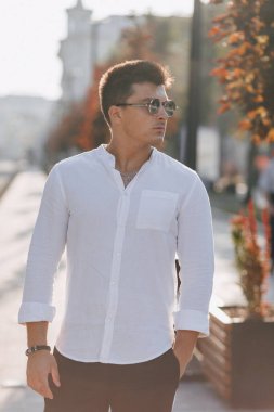 Sıcak ve güneşli bir günde Avrupa sokaklarında yürüyen beyaz tişörtlü şık bir genç.