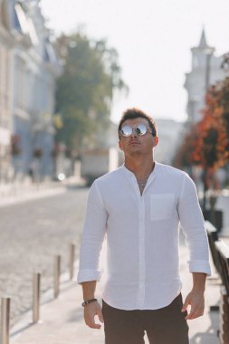Sıcak ve güneşli bir günde Avrupa sokaklarında yürüyen beyaz tişörtlü şık bir genç.