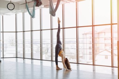 Konforlu, genç ve çekici bir kız, panoramik pencerelerin arka planında yoga yaparak spor yapıyor.