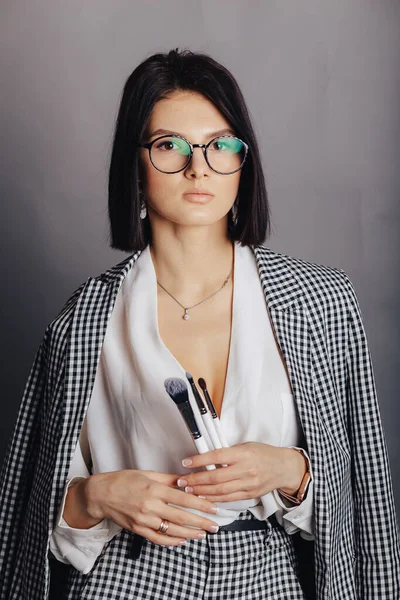 Stüdyoda karanlık arka planda poz veren iş elbiseli çekici bir genç kız. Şık kıyafetler ve entelektüellik kavramı.
