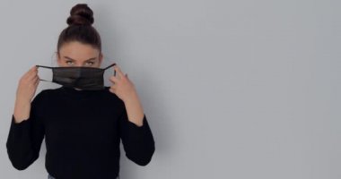 Basit bir ışık arka planında koruyucu maskeli bir kız. Çıkar ve maskeyi tak. Virüslere ve kirli havaya karşı koruma.