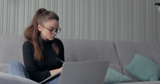 Дівчина працює на ноутбуці вдома на дивані. залишатися вдома і працювати віддалено. ізоляція вдома . — стокове відео