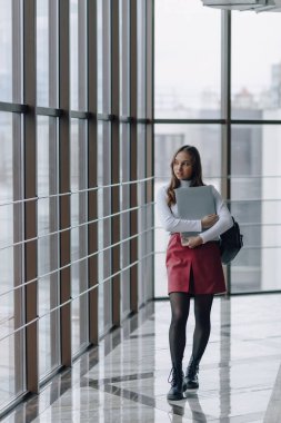 Çekici bir kız, havaalanı terminalinde ya da ofiste dizüstü bilgisayarla parlak bir koridorda yürüyor. seyahat atmosferi ya da alternatif çalışma ortamı. Serbest çalışan öğrenci, teknolojiyle iş toplantısına gidiyor..