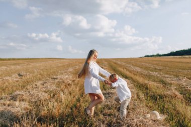 Sarışın küçük çocuk samanlı, beyaz saçlı annesiyle oynuyor. Yaz, güneşli hava, çiftçilik. Mutlu çocukluk. aile.