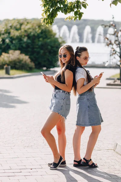 Duas Meninas Bonitas Passeio Parque Com Telefones Dia Ensolarado Quente — Fotografia de Stock
