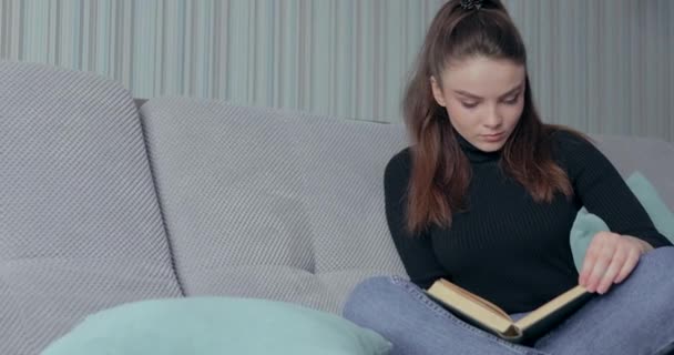 Menina bonita lendo um livro no sofá. fique em casa e relaxe. auto-desenvolvimento. livro de papel . — Vídeo de Stock