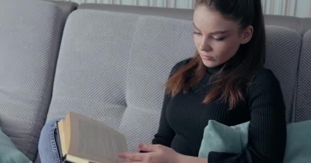 Gadis cantik membaca buku di sofa. tinggal di rumah dan bersantai. pengembangan diri. buku kertas. — Stok Video