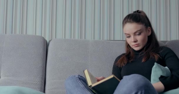 Ładna dziewczyna czyta książkę na kanapie. Zostań w domu i odpręż się. rozwój własny. papierowa książka. — Wideo stockowe