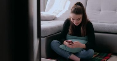 Laptopun arkasında elinde telefonla sıcak çay içen bir kız. Evde kalmaktan yorgun düştüm. Evden izolasyon ve iş.