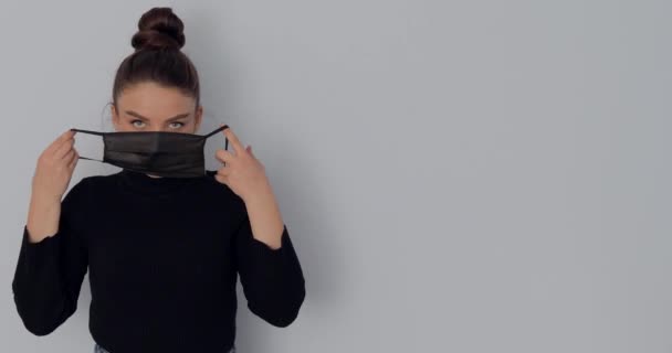 Menina em uma máscara protetora em um fundo leve simples. remove e coloca a máscara. proteção contra vírus e ar sujo . — Vídeo de Stock