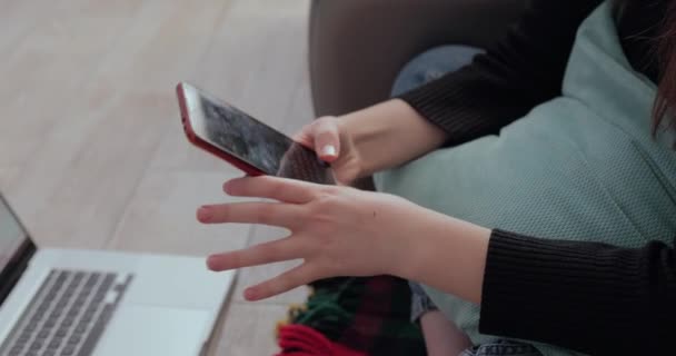 Ragazza primo piano bere tè caldo con il telefono in mano dietro il computer portatile. stanchezza di stare a casa. isolamento e lavoro da casa . — Video Stock