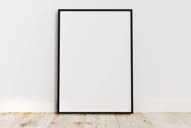 Empty thin black frame on light wooden floor with white wall behind it. Empty poster frame mockup. Empty picture frame mockup. Blank photo frame.