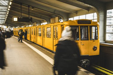 Berlin 'deki metro istasyonu, sarı tren ve yolcularla dolu. Berlin 'de toplu taşıma. Berlin konseptinde seyahat ve turizm.
