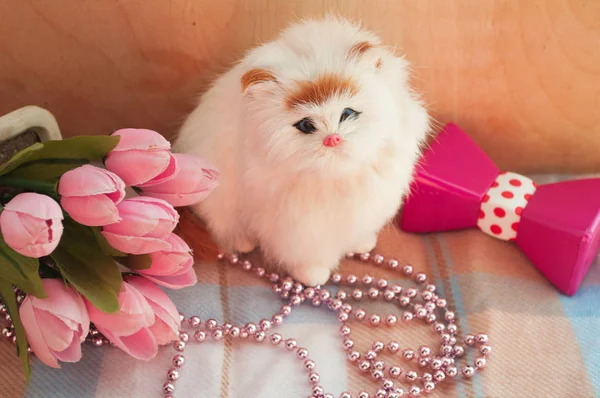 fluffy toy cat on a background of pink beads and flowers