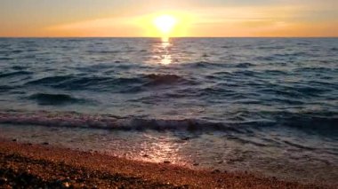 Kumlu bir sahilde gün batımında güzel bir deniz manzarası. Sıcak güneş ışığı sudaki bir yol tarafından yansıtılır..