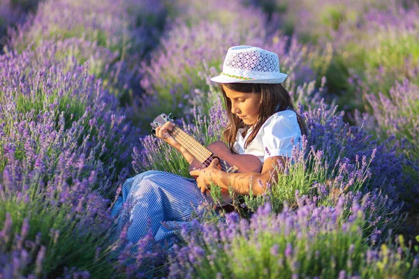 Şapkalı güzel bir köylü kızı lavanta tarlasında otururken küçük bir gitar çalar.
