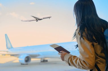 Pasaport ve uçuş kartlarını elinde tutan kadın yolcu terminalde yolcu alımı için beklemede. Uçak terminale yanaşıyor.