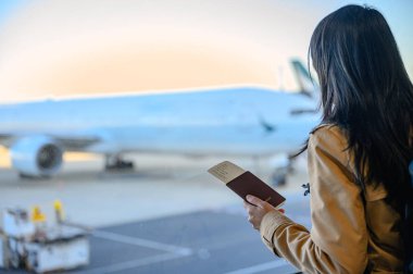 Pasaport ve biniş kartı, yolcu girişi için hazır bekleyen yolcu kadının elinde. Terminale yanaşan uçak, bakım hizmetlerinde gecikme ya da zaman aşımına uğramayı bekliyor.