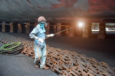 worker, paint man, working for repainting after sand blasting of the bottom layer of the commercial ship in floating dock yard by spraying paint machine