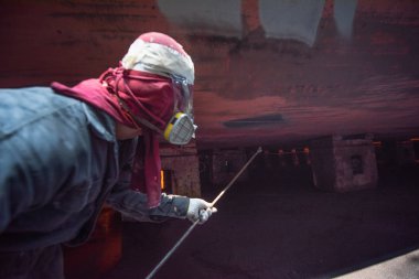 Painting area spraying by worker, paint man, working for repainting after sand blasting of the bottom layer of the commercial ship in floating dock yard by spraying paint machine