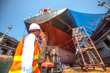 Stevedore, kontrolör, liman amiri, yüzen kuru rıhtımdaki ticari kargo gemisinin kıç tarafındaki tadilat ve boyama onarımını, kuru tersanede kum patlamasını inceleyin.