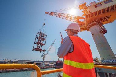 stevedore or foreman, engineering, loading master talks to crane driver by walkie talkie for safety lifting  the goods shipment, lifting by gantry crane, working at risk on the high level insurance