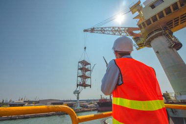 Liman işçisi ya da ustabaşı, mühendis, vinç sürücüsüyle konuşuyor güvenlik için telsizle mal ya da sevkiyat için, vinçle kaldırılıyor, yüksek seviyede sigorta riskiyle çalışıyor.
