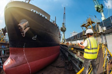 Gemi vinci tarafından yüklenen konteynır ünitesi, liman terminaline naklediliyor, liman işçisi çalışıyor, lojistik ve ulaşım hizmetleri dünya çapında küresel taşımacılık