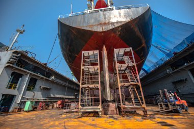 aft of commercial general bulk cargo ship in floating dry dock yard, sitting on concrete supporters for recondition, repairing, painting overhaul dock yard