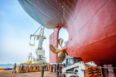 over hull dry dock of the commercial ship under repairing, recondition, painting and cleaning in dock yard, Aft stern bottom of the ship laying on the structure support in floating dry dock
