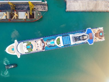 aerial top view of the passenger cruise vessel ship is in the port, arrival and departure of the ship under command and navigation by pilot and captain, withn tug boat assist for safety attending