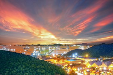 in between the hills, container storage yard conneting to sea port terminal, export and import commercial industrial estate zone, sunset skyline in background