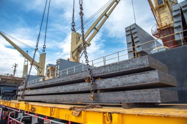 bundle of steel slabs being loading discharging in port terminal, laying onto base of trailer, release unhook,disconnected chain lashing, handle by gang of stevedore labor , shipment cargo in transition from land and sea transport services