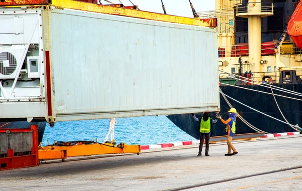 stevedore labor working on fitting container shoe to locking cone ready to loading and accomodate on the bay of the ship