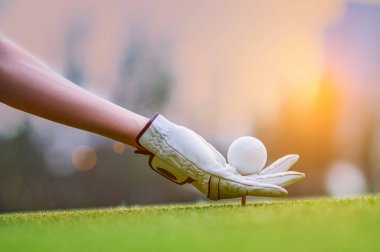 golf ball in hand of woman golf player laying on wooden tee on TEE-OFF with light of sunset in background