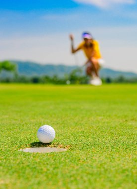 golf ball run through almost success drop to hole on the green with exciting watching by woman golf player in background