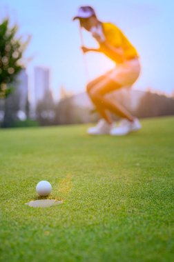 young woman golf player mostly success to putting golf ball into the hole on the green of the golf course, cheerfully of woman golf player in background