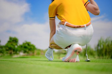 Golf sahasının yeşilini takmak için elinde golf topu tutan bir kadın golfçü.