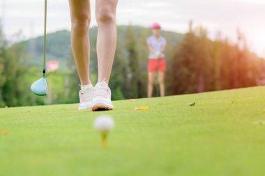 Kadın golfçü kontrol çizgisinde topa vuracak, topa vurmak için sırayla yürüyecek hedefi kontrol edecek, rakip rakip ya da arka planda golf arkadaşı izleyecek.