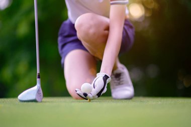 Golf topu tutan genç bayan golfçünün eli hedefe giden topa vurmaya hazır olan ahşap tişörte bastırıyor.