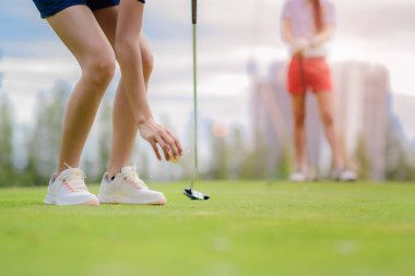 Kadın golfçü sahada bir golf topu kuruyor. Gün ışığında kazanmak için topu deliğe sokuyor.