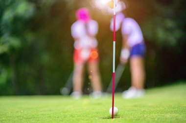 Golf sahasının yeşilindeki delikten koşan kadın golfçü tarafından vurulan ya da vurulan golf topu golf topunun hedefini ıskaladı.