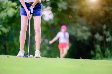 Golf sopası tutan genç bayan golfçünün eli golf sahasına vurması için arka plandaki yeşil, rekabetçi ya da golfçü oyuncuyu tutuyor.