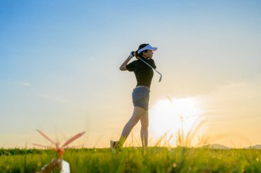 Golf oynayan kadın golfçü, golf topunu vurduktan sonra atış sahasından hedefe kadar yeşil, gün batımında çim yolu.