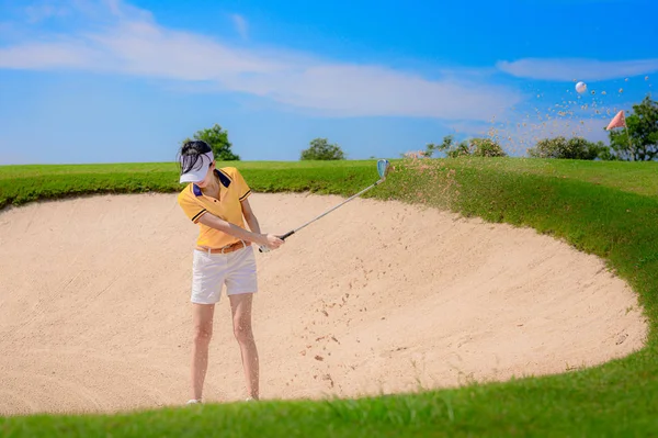 Woman golf player in action of hitting golf ball away from a trouble sandbank bunker in golf course, trouble away keep going concentrate to final destination